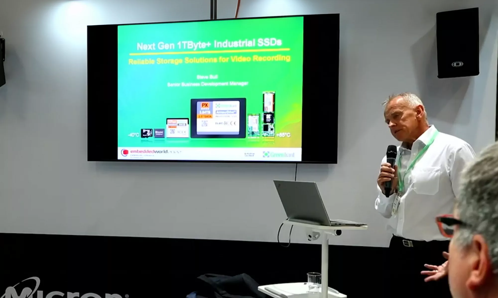 男子拿著麥克風在演講，背景為綠色螢幕